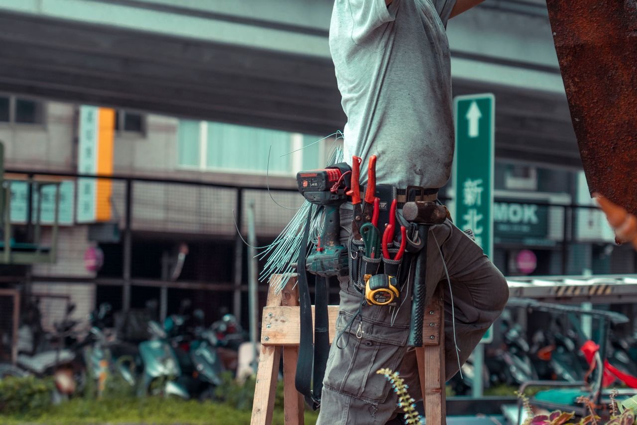 Crafting Captivating Headlines: Your awesome post title goes here Handyman standing on a ladder with tool belt, repairing outdoors with visible tools.