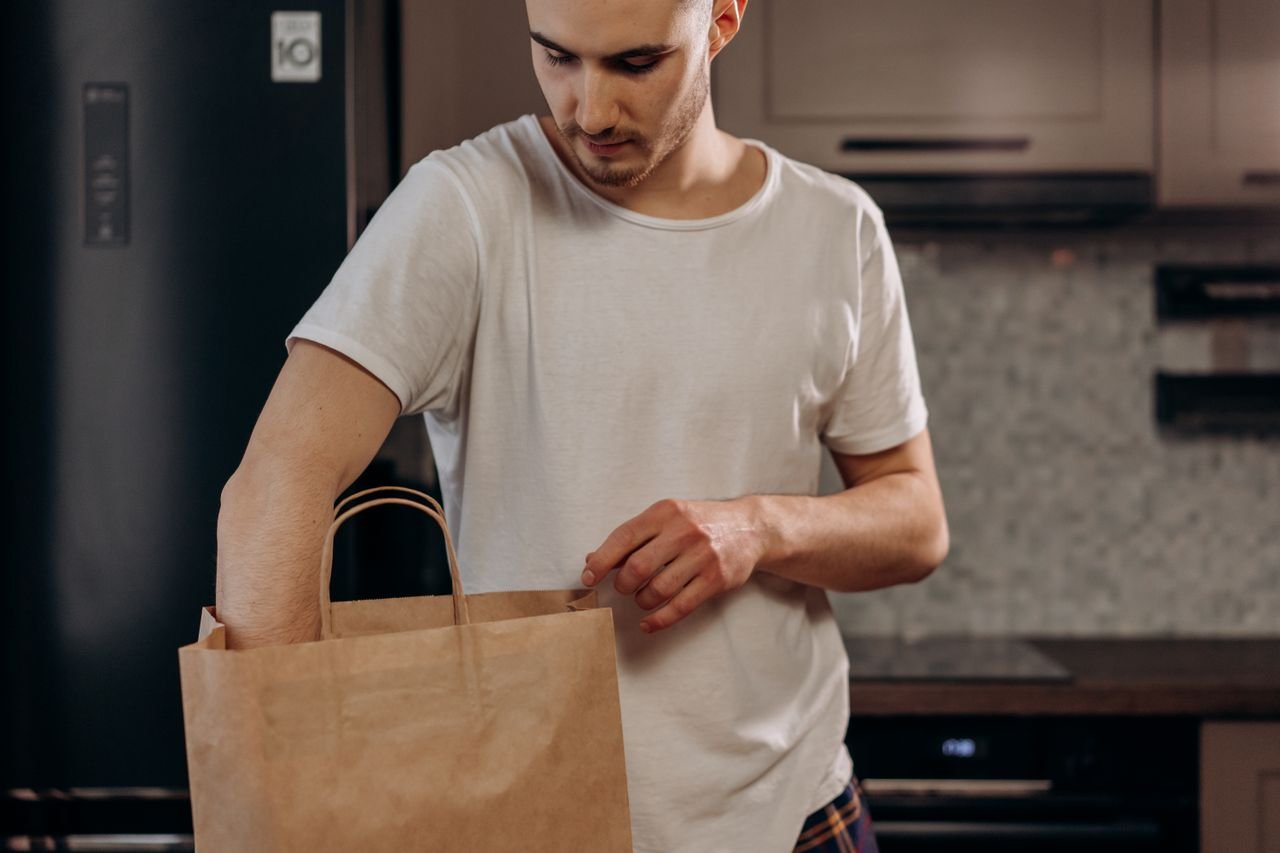 Mastering the First Impression: Your intriguing post title goes here Male in white shirt unpacking groceries from paper bag in contemporary kitchen setting.